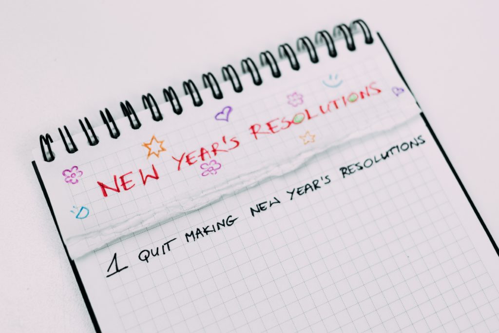 Notebook titled "New Years Resolutions" with list, "1. Quit Making New Year's Resolutions"